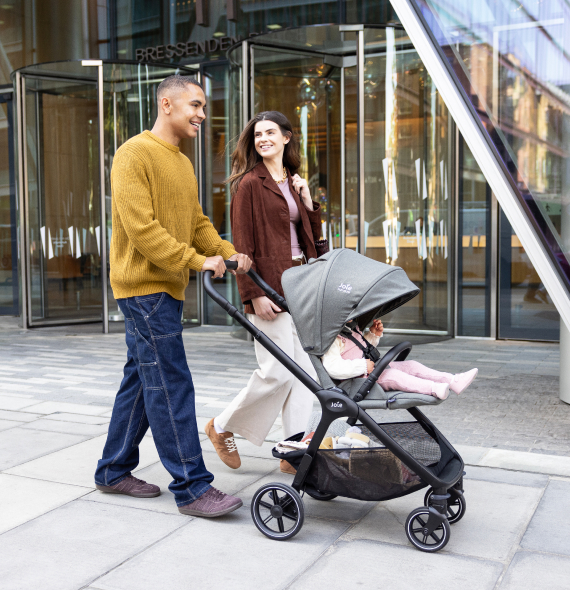 Un couple de jeunes parents marche en ville avec sa poussette Joie