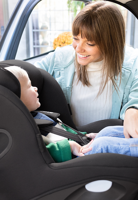 Une maman installe son enfant dans un siège auto, harnais ajusté
